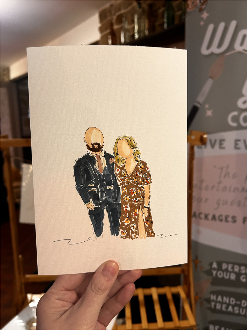A hand holding a hand-painted couple portrait at a wedding